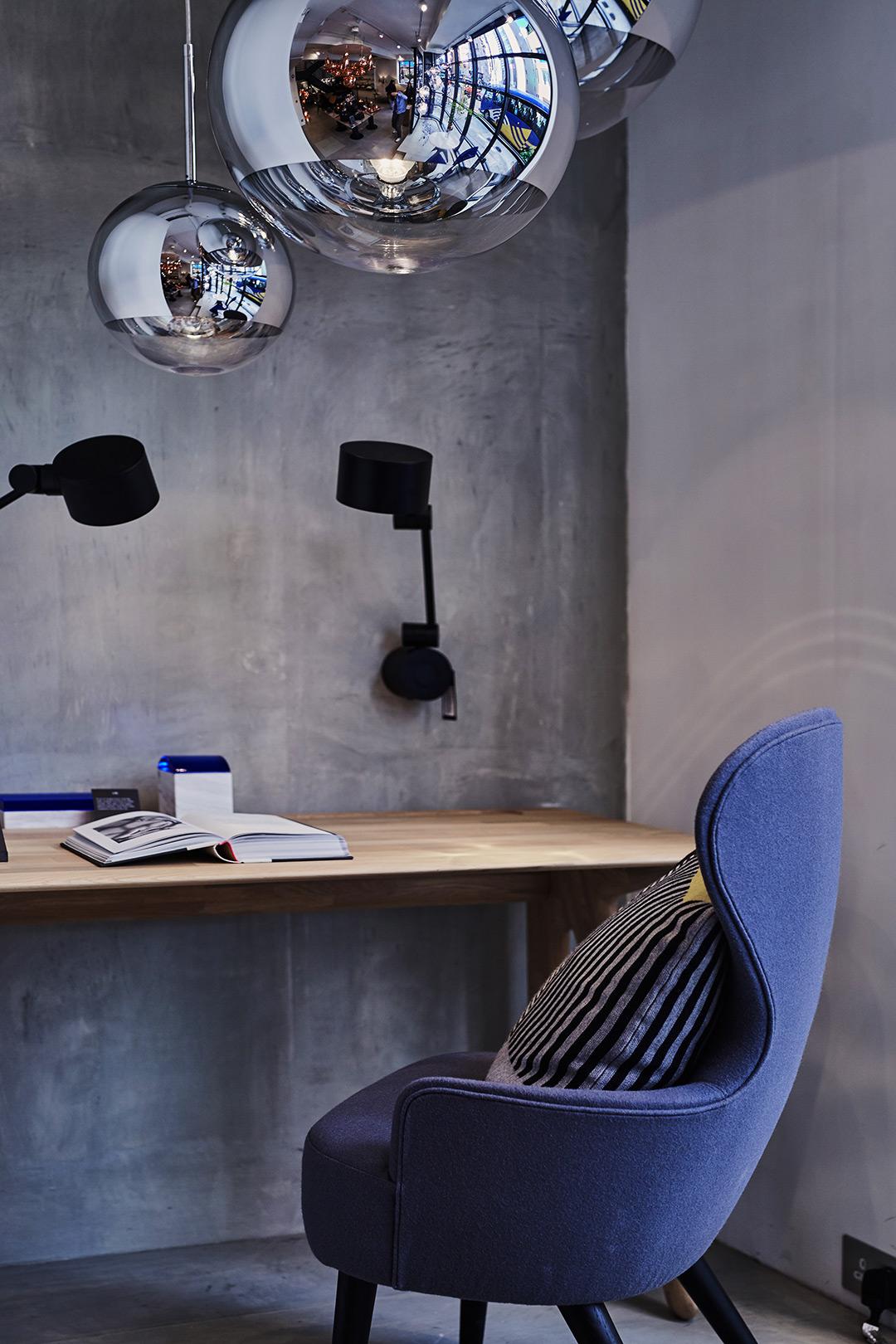 Minimalist desk with blue chair, concrete wall, and hanging decorative lights