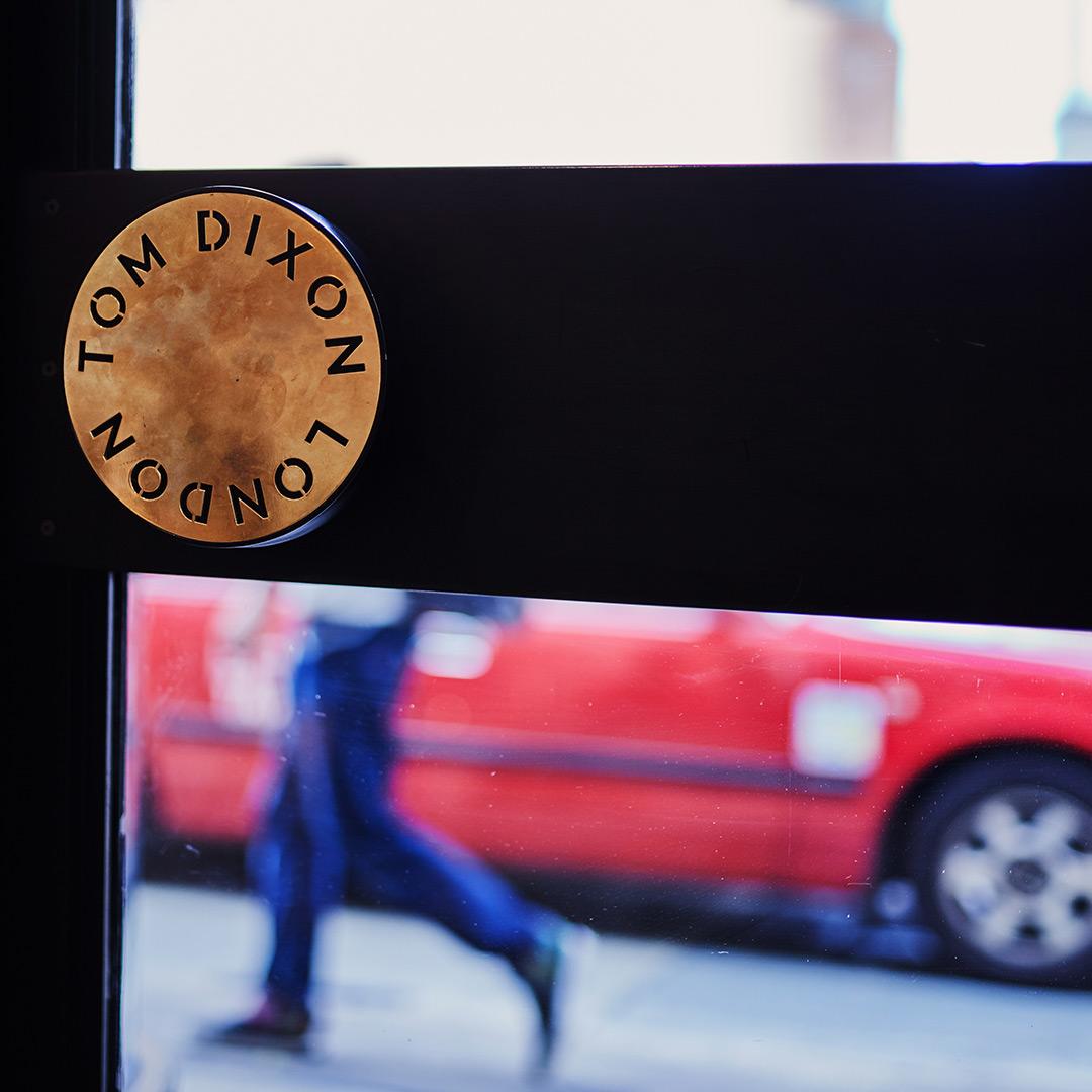 Close-up of Tom Dixon Hong Kong store sign with pedestrian and red car in background