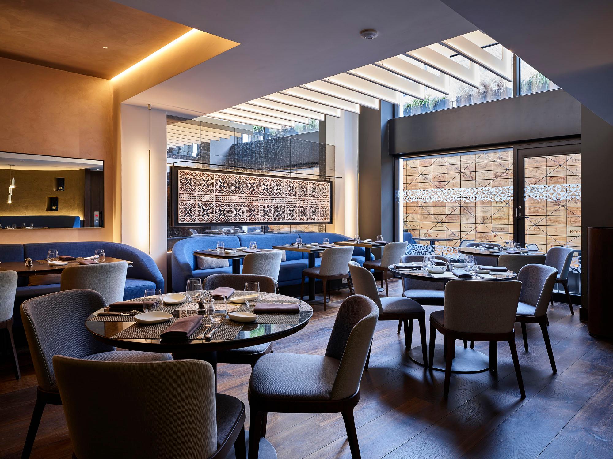 Elegant restaurant interior with round tables, upholstered chairs, and large windows with natural light