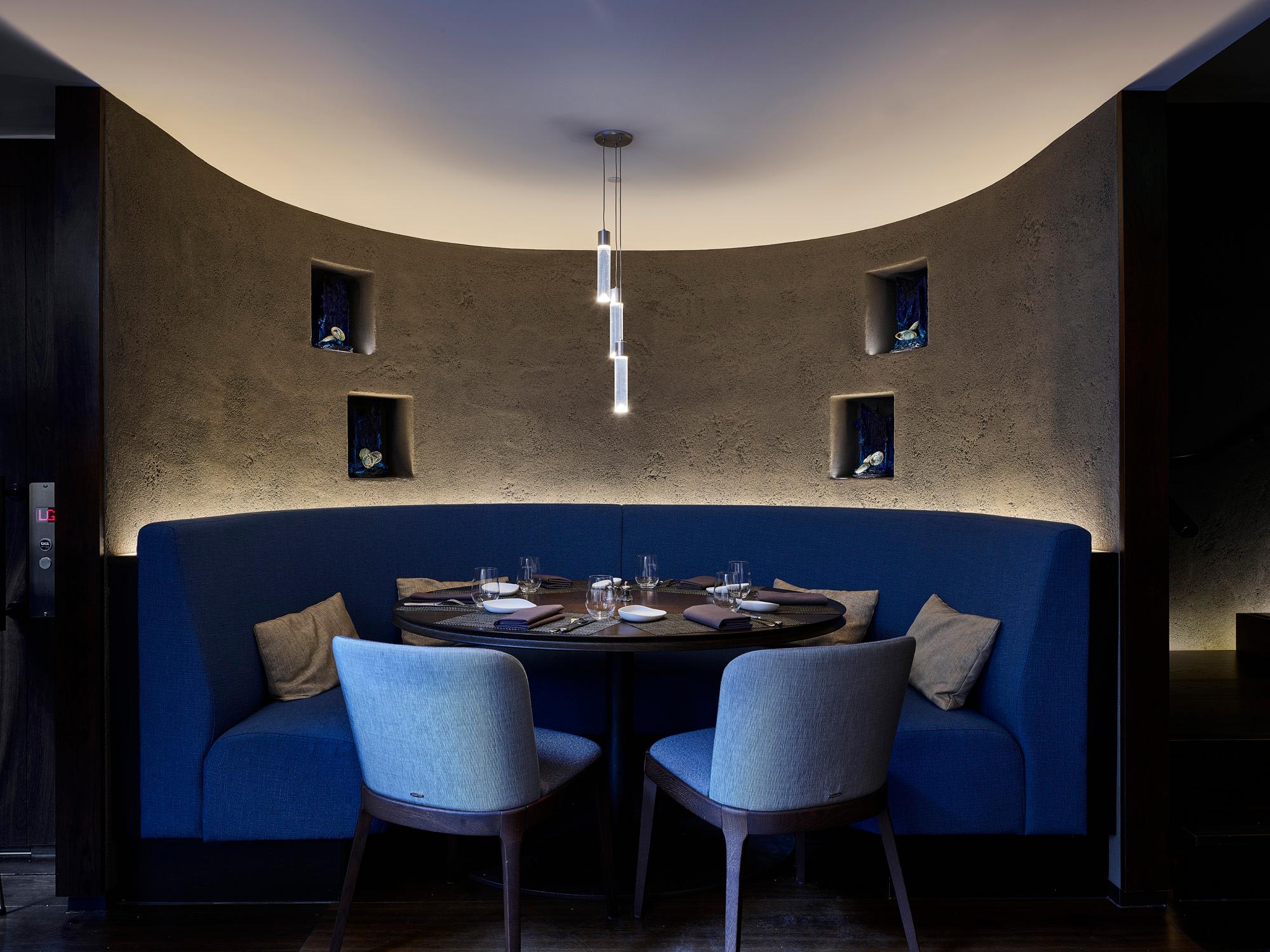 Modern restaurant dining area with acoustic ceiling panel, round tables, and stylish blue chairs